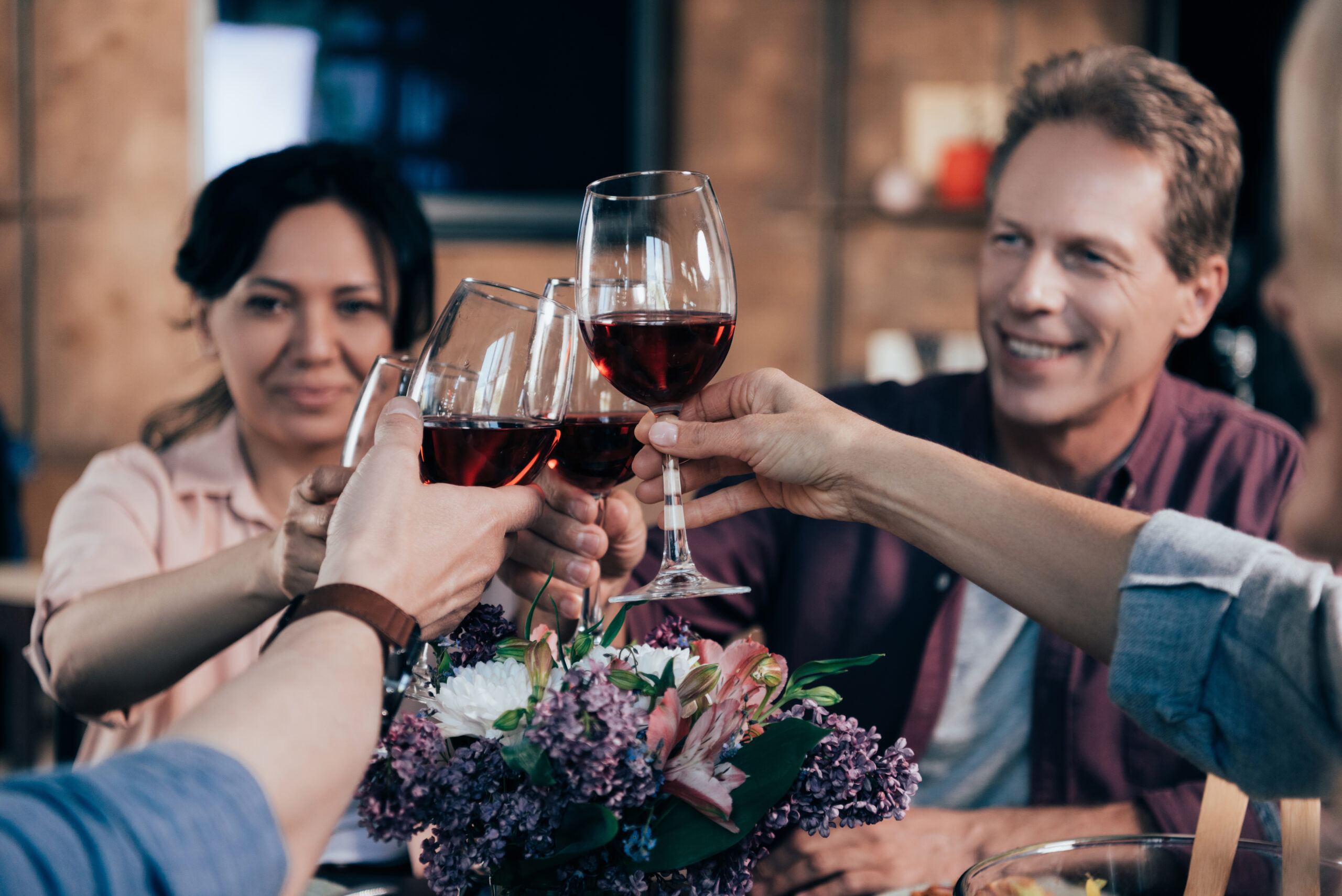 cropped shot of happy friends drinking wine while having dinner together